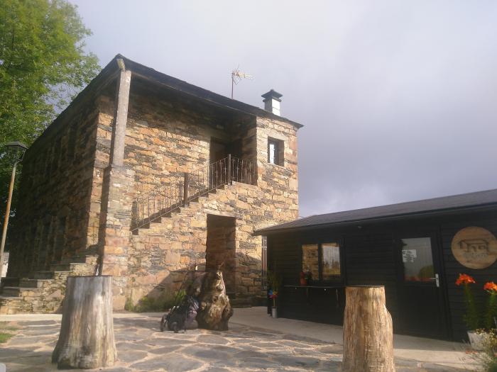 Ein Steinhaus mit zwei Stockwerken und Flachdach sowie einer Außentreppe aus Stein direkt davor; ein einstöckiges Holzhaus rechts daneben.