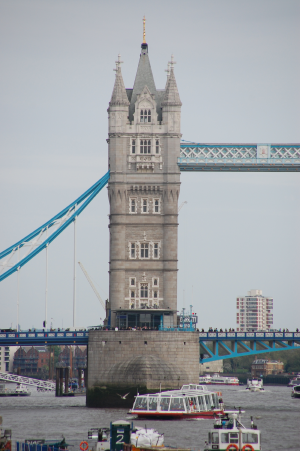 Ein Teil der Tower Bridge, man sieht einen der Türme in der Bildmitte. Die Streben leuchten türkis. Viele Menschen sind auf der Brücke.