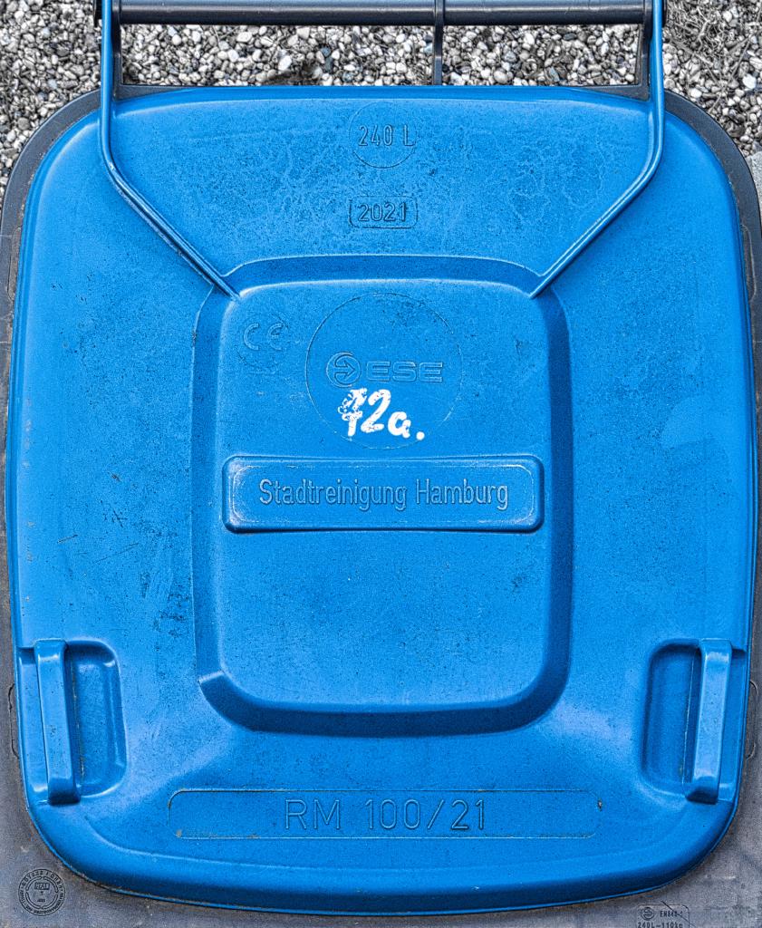 Eine Mülltonne mit blauem Deckel, direkt von oben fotografiert. Es steht 'Stadtreinigung Hamburg' in der Mitte, '2021' und '240l' oben sowie 'RM 100/21' unten auf dem Deckel gedruckt. Handschriftlich steht in weiß zusätzlich '72a' zwischen 'Stadtreinigung Hamburg' und dem Logo des Tonnenherstellers geschrieben.