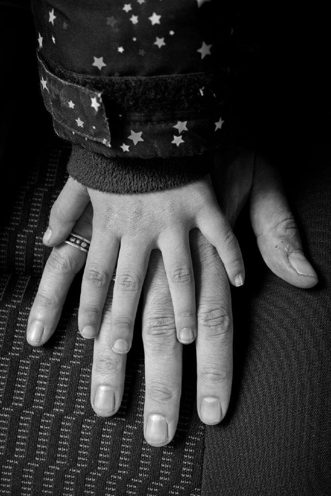 Zwei Hände übereinander. Unten eine männliche, darüber eine kindliche, deutlich kleinere Hand. Ein Ansatz von Kinderjacke mit Sternen ist erkennbar. Das Foto ist in Schwarzweiß.