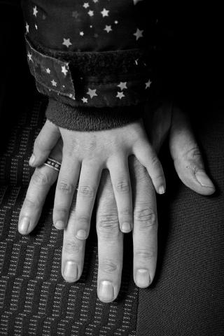 Zwei Hände übereinander. Unten eine männliche, darüber eine kindliche, deutlich kleinere Hand. Ein Ansatz von Kinderjacke mit Sternen ist erkennbar. Das Foto ist in Schwarzweiß.