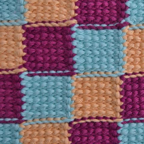 Eine Nahaufnahme eines Strickstoffs mit einem sich wiederholenden Schachbrettmuster aus abwechselnd hellblauen, zartorangefarbenen und tiefmagentafarbenen Quadraten.