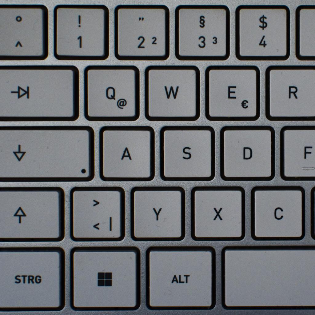 Nahaufnahme der linken Hälfte einer hellgrauen Computertastatur mit deutschem Layout: von oben nach unten die Zahlenreihe bis 4, die Tasten Tab, Q, W, E, R, Feststelltaste, A, S, D, F, Umschalt, Y, X, C sowie STRG, Windows-Taste und ALT. Auf einigen Tasten liegen feine Staubkörnchen.